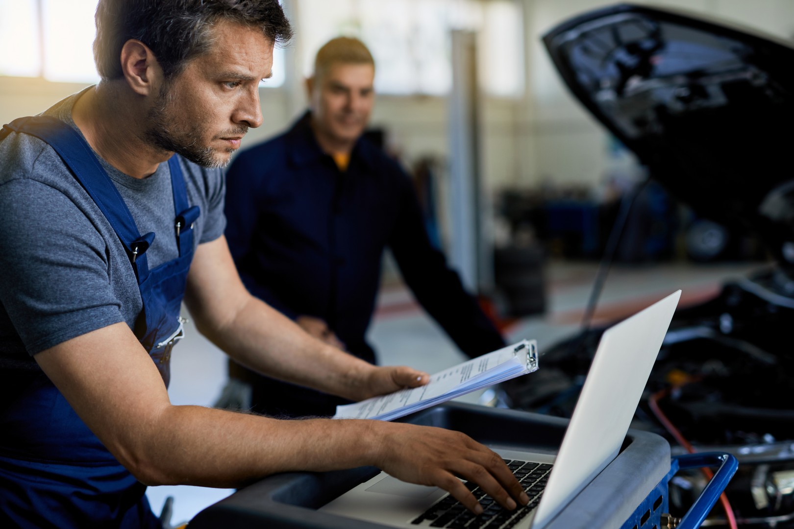 Tecnico d'officina e consulente al computer accanto a un'auto col cofano aperto